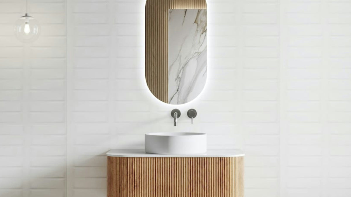 Bathroom with wooden vanity and oval mirror against a white tiled wall.