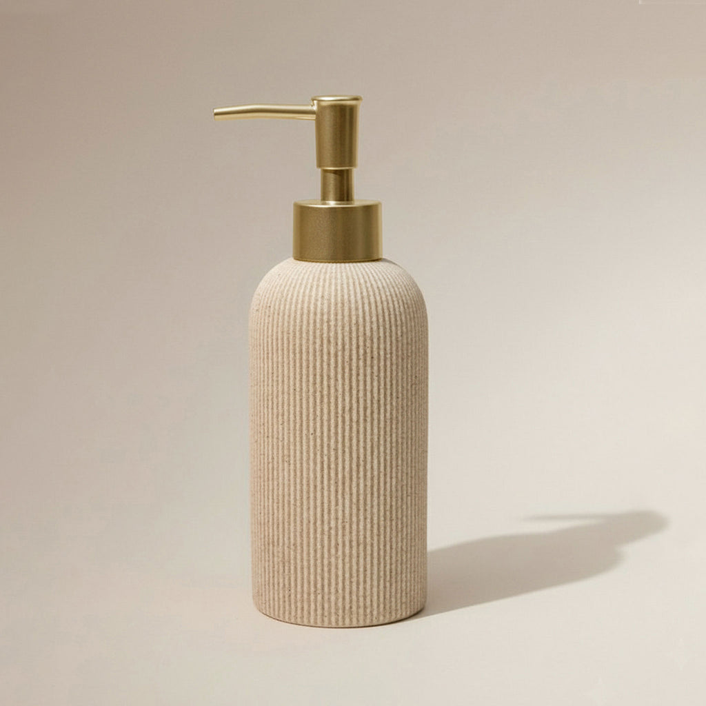 A ribbed beige dispenser bottle with a brushed gold pump shown on a warm beige background with a soft shadow.