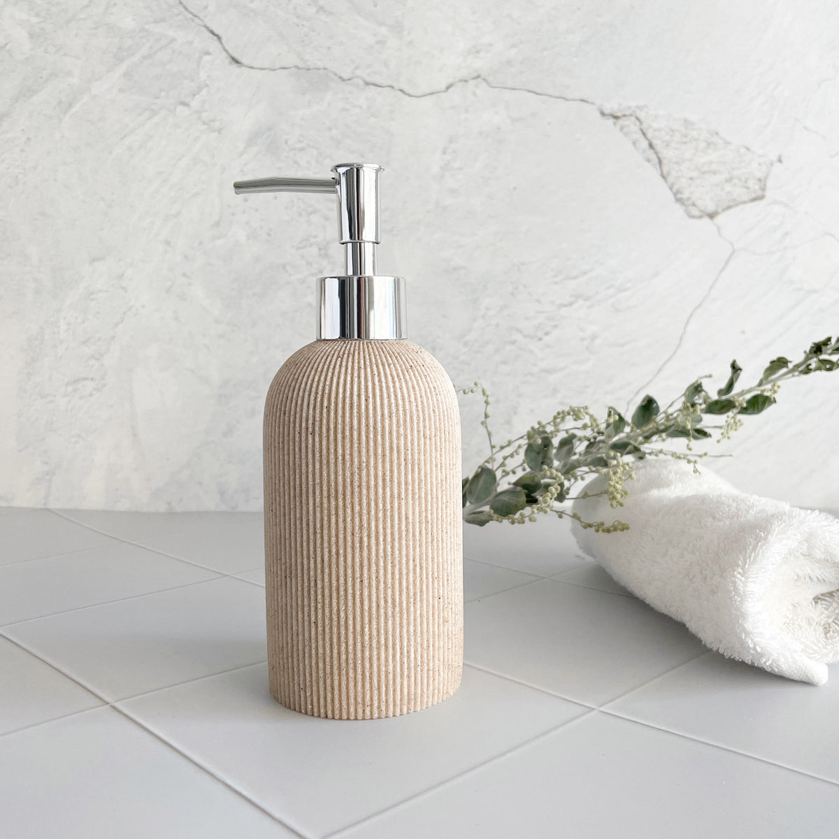 Beige soap dispenser with silver pump on a light gray tiled floor.